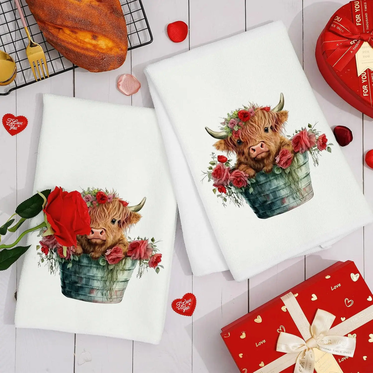 A set of two white kitchen towels featuring a watercolor illustration of a Highland cow in a floral planter.