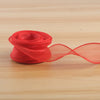 A roll of red satin ribbon, 40mm wide, lying on a wooden surface.