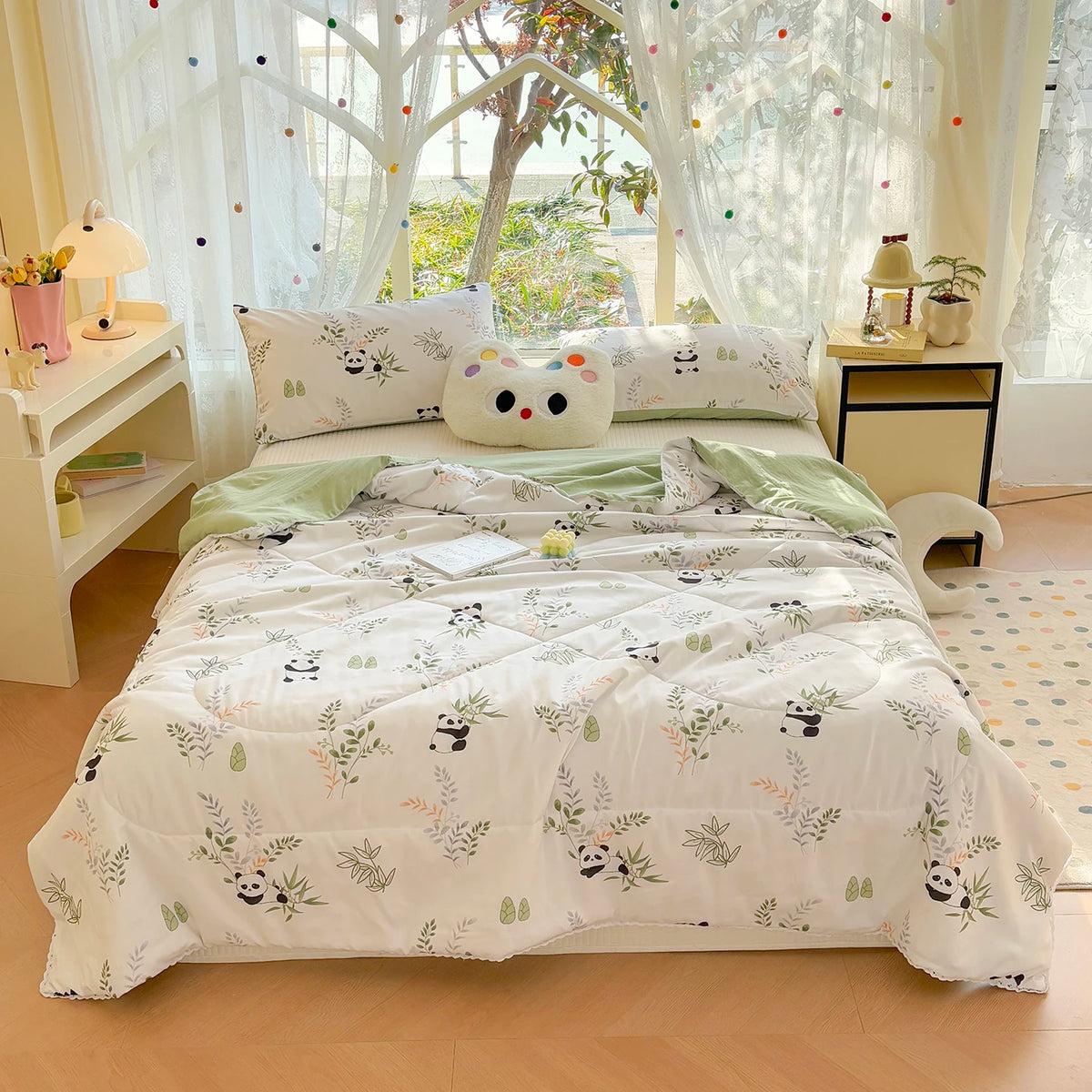 A white comforter with a panda print pattern and lace trim is displayed on a bed surrounded by light curtains and decorative 