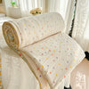 A rolled cream colored quilt with multicolored polka dots resting on a white fabric surface near sheer curtains.