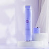 A tall purple electric shaver standing on a white cylindrical stand next to a white round platform.