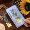 A vintage metal bookmark with an artistic hollow design and purple tassel resting on a wooden surface next to a sunflower.