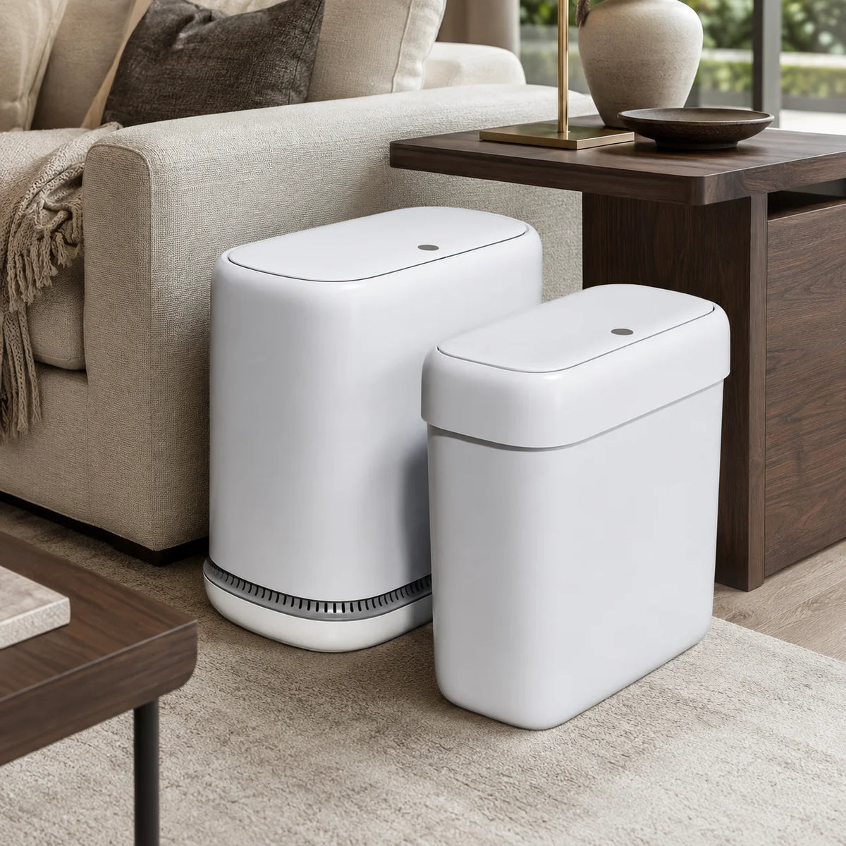 A white, slim rectangular trash can set with lids is displayed on a wooden table next to a sofa.