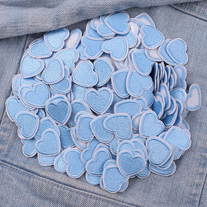 A pile of light blue heart-shaped embroidered iron-on patches for DIY clothing decoration