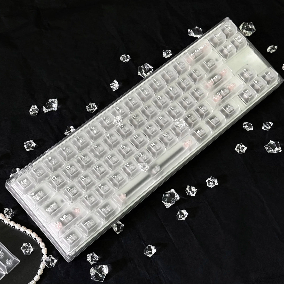 A translucent PC keycap for a mechanical keyboard lying on a black surface with scattered clear crystals.