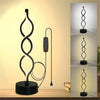 A black, seaweed-shaped desk lamp with a soft ambient glow is displayed on a wooden surface.