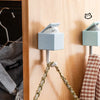 A light blue cat-shaped adhesive hook is mounted on a wooden cabinet door, hanging from a gold chain.