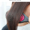 A person is using a black hair brush with natural bristles to clean dandruff from dark brown hair.