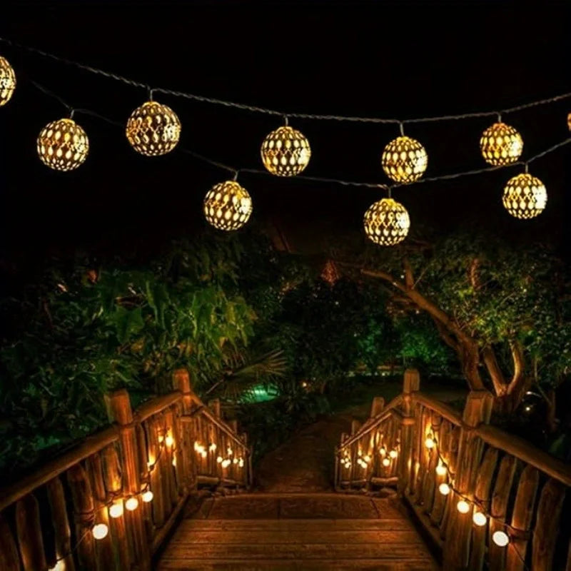 String lights illuminate a wooden walkway surrounded by lush greenery at night.