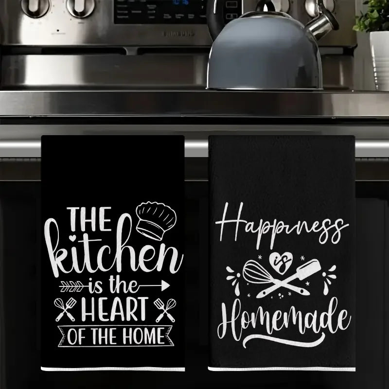 A set of two black kitchen towels featuring the slogan The kitchen is the heart of the home.