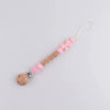 A pink silicone pacifier clip with a wooden baby name charm and a pink bow on a gold lanyard.