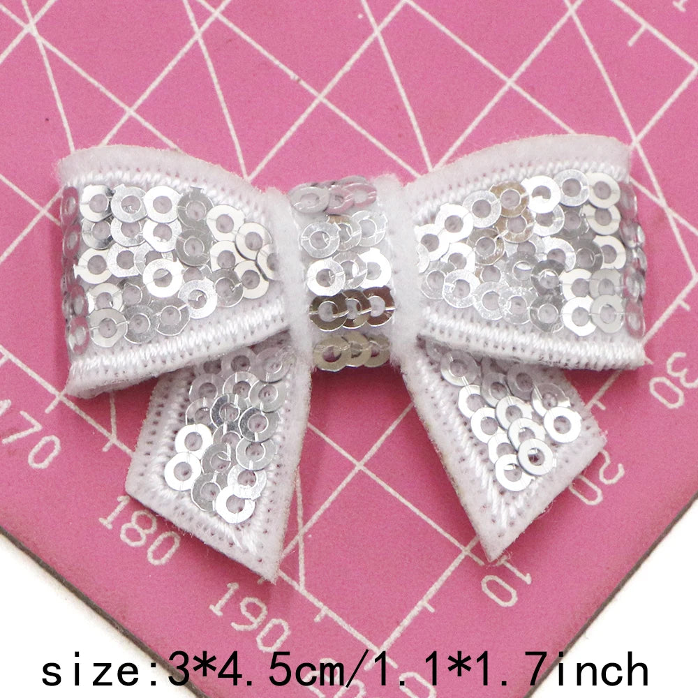 A white sequin bow patch is shown against a pink grid background.
