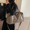 A woman holds a tan leopard print duffle bag with a leather strap against a light wall.