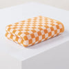 A stack of soft plaid cotton bath towels in a warm orange and cream checkered pattern.