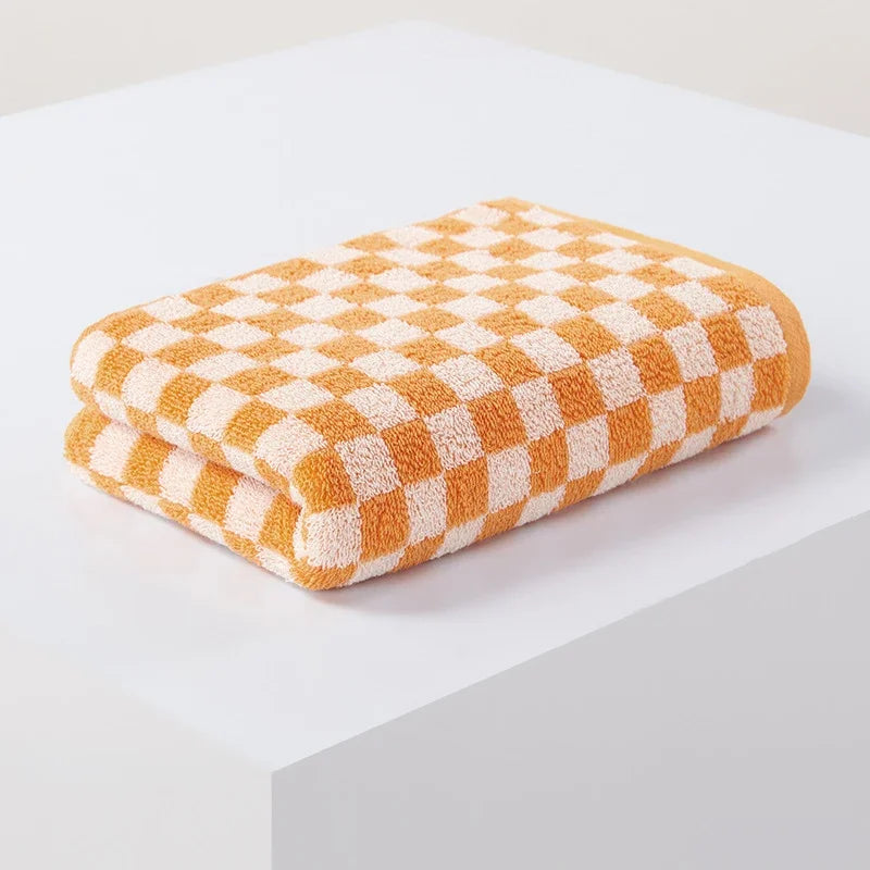 A stack of soft plaid cotton bath towels in a warm orange and cream checkered pattern.