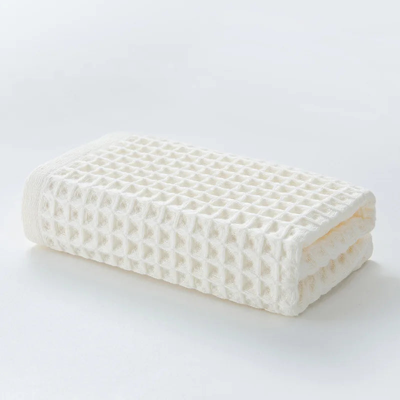 A rectangular white waffle weave bath towel folded neatly on a white surface.