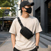 A young man wearing a black tactical MOLLE waist pack and a black face mask, standing outdoors.