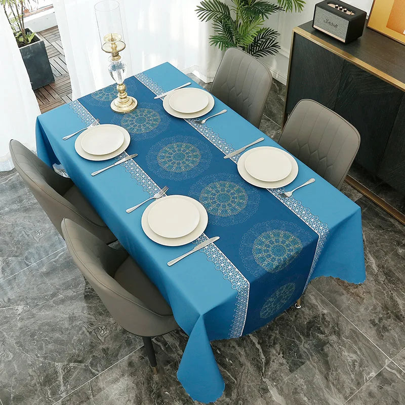 A long blue tablecloth set for a dinner table with white plates and silverware, featuring a geometric pattern.