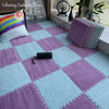 A close-up of soft purple and light blue interlocking plush floor tiles on a wooden floor with pillows and a decorative statu