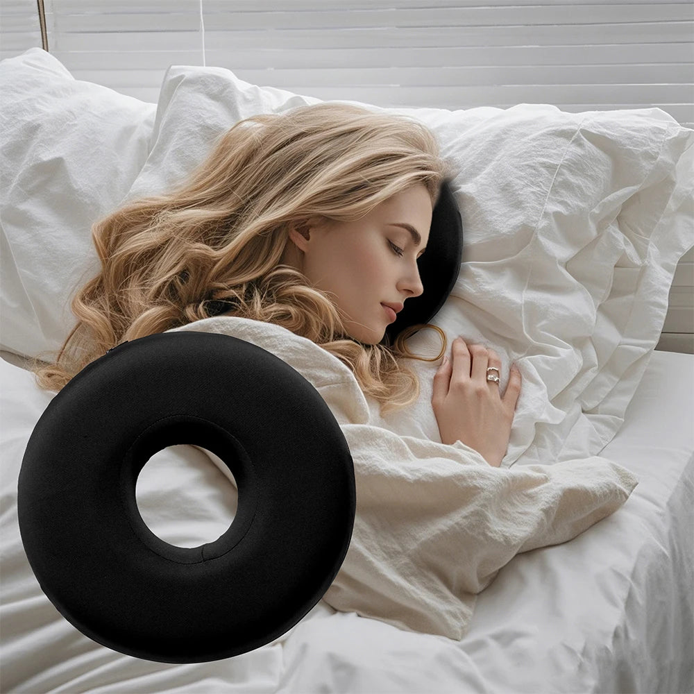 A blonde woman rests her head on a black memory foam ear piercing pillow in a white bed.
