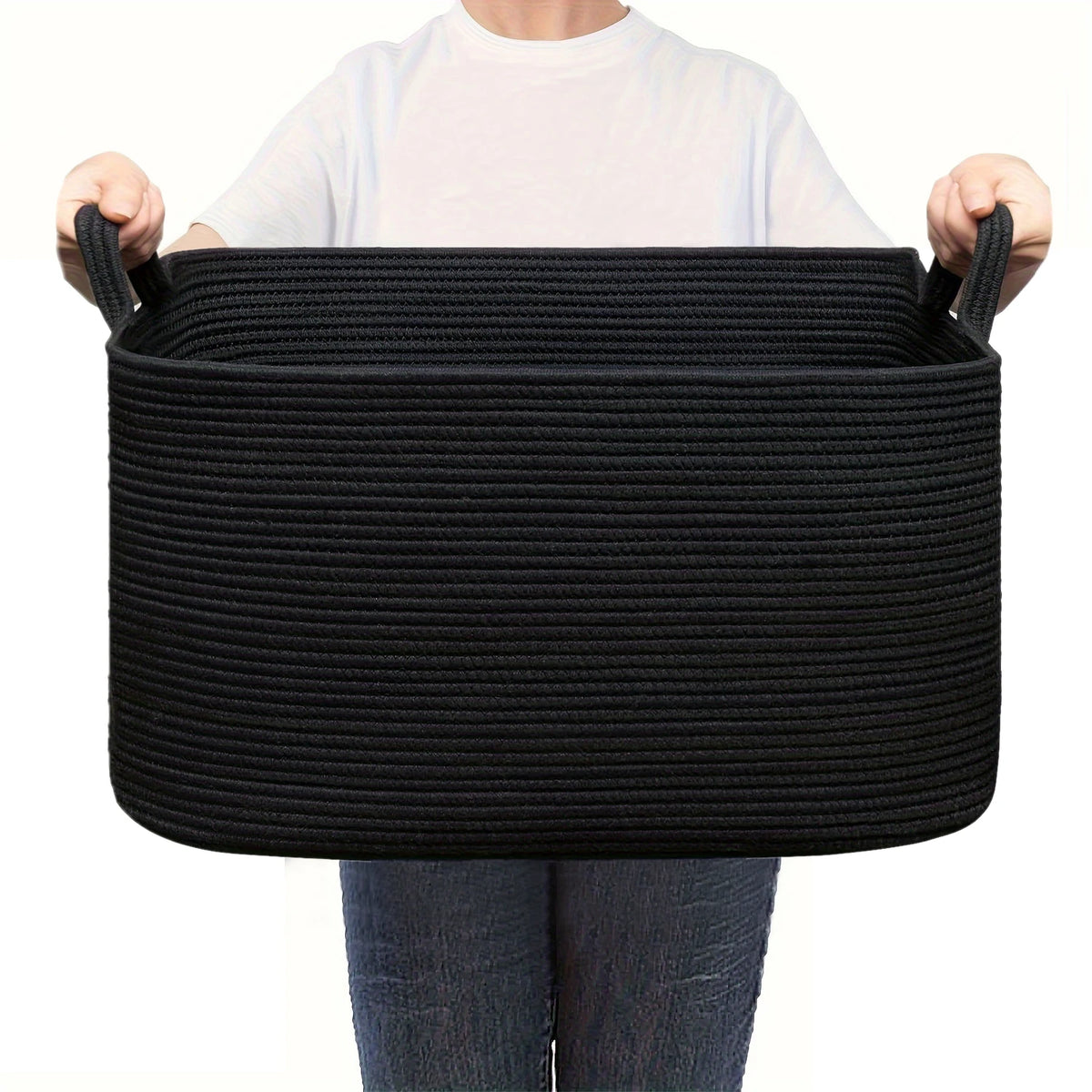 A person holds a black woven cotton rope storage basket with handles.