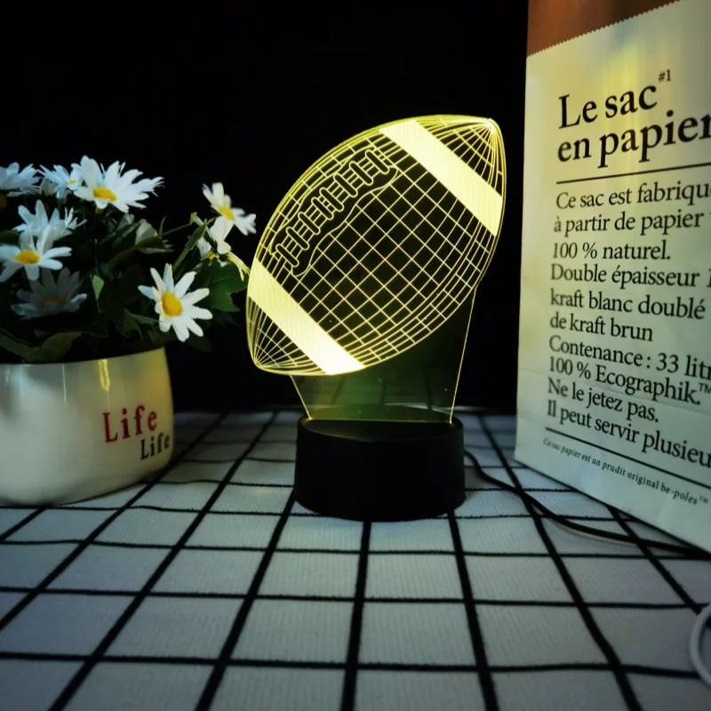 A yellow sports-themed night light with a mesh pattern sits on a white surface next to a potted plant.