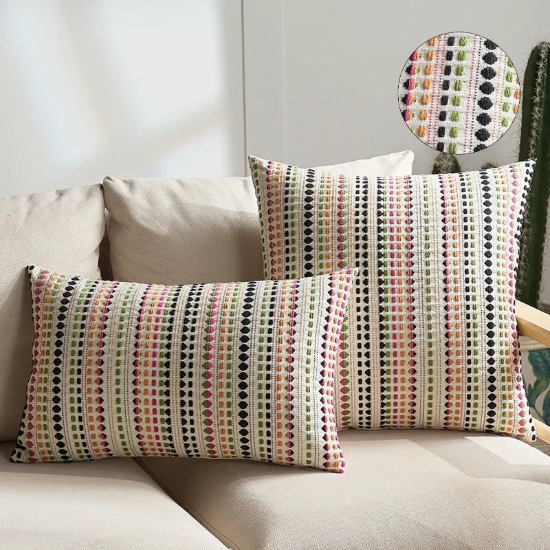 A set of two bohemian linen pillow covers featuring a multicolored geometric pattern on a light beige sofa.