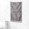 A gray wall-mounted laundry storage bag with a circular opening hangs against a white marble tile background.