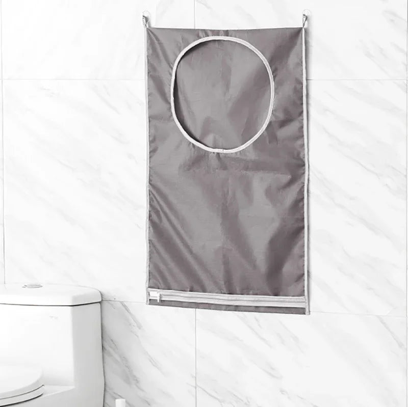 A gray wall-mounted laundry storage bag with a circular opening hangs against a white marble tile background.