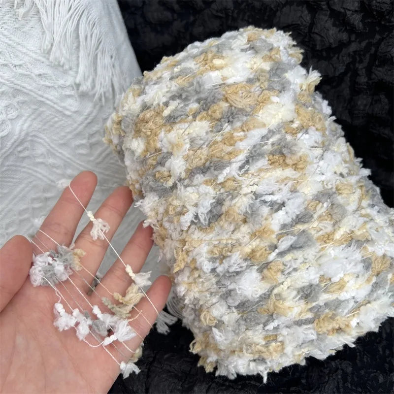 A ball of hand-dyed variegated cotton blend yarn in gray and cream colors resting on a dark surface.
