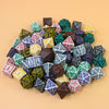 A collection of multi-sided polyhedral dice in various colors and shapes scattered on a light background.