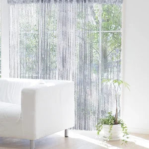 A sheer silver tassel string curtain hangs in a window, filtering natural light and creating a soft, textured drape.