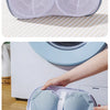 A hand places a light blue mesh laundry bag for delicates onto a white washing machine.
