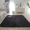A black faux fur accent rug placed on a light wood floor in a bright, minimalist room.