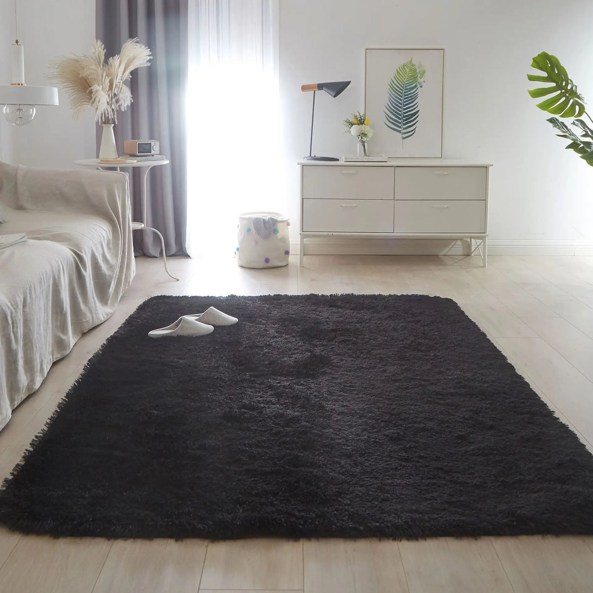 A black faux fur accent rug placed on a light wood floor in a bright, minimalist room.