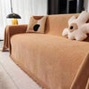 A tan chenille sofa throw draped over a sofa, featuring a light beige textured fabric and tassel edges.