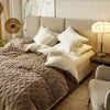A luxurious beige duvet cover and blanket with a quilted texture is displayed on a bed in a bright room.