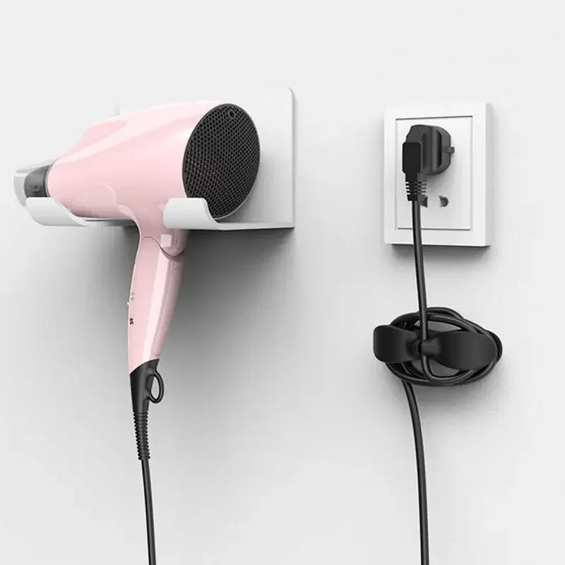 A pink cord organizer and wire winder is mounted on a white wall, showing its attachment to a power outlet.
