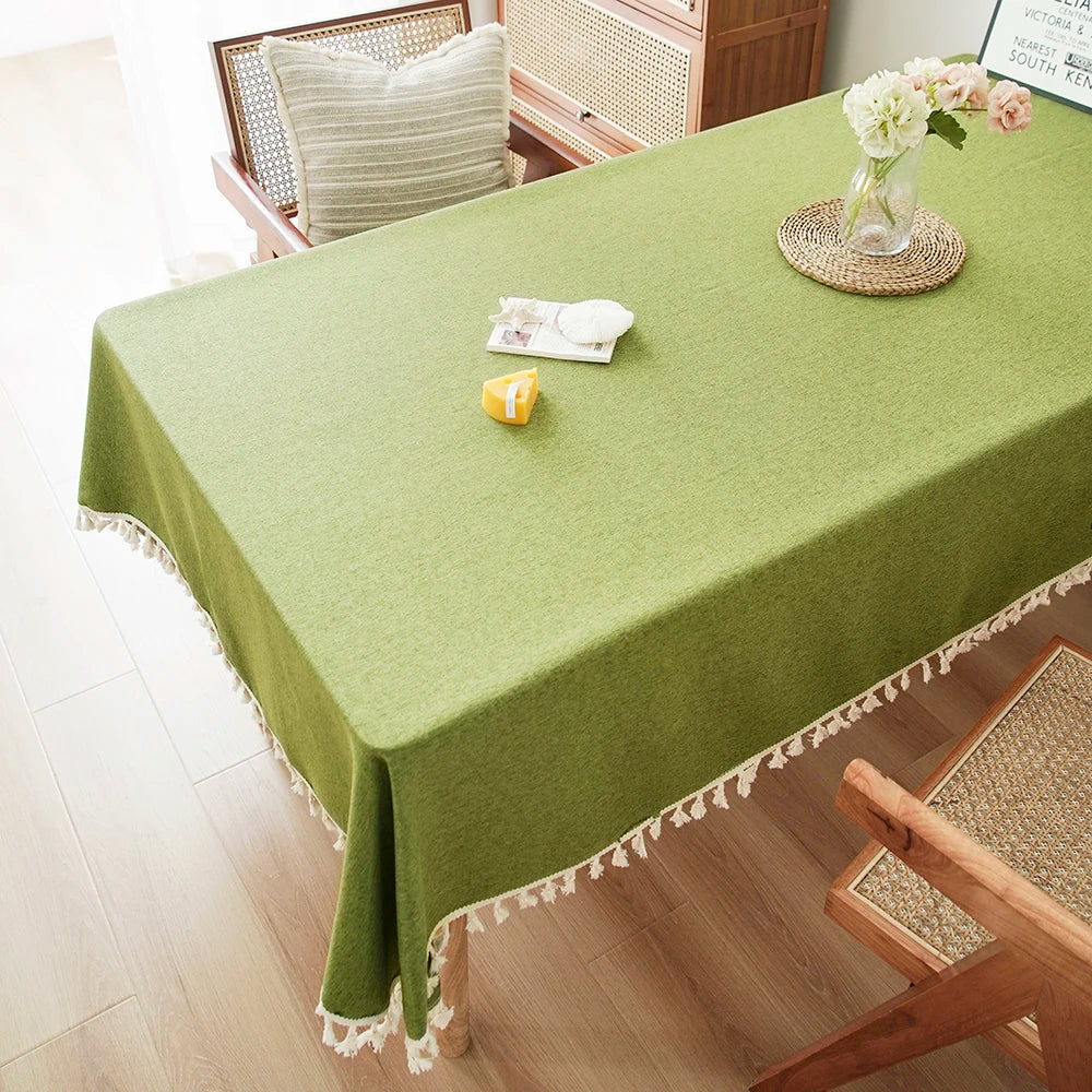A lime green farmhouse tablecloth with white cotton tassels covers a dining table.