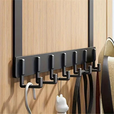 A black over-the-door coat rack with six hooks mounted on a light wood panel.