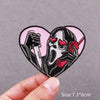 A black and white embroidered skull horror patch with red eyes and a screaming expression on a pink heart shape.