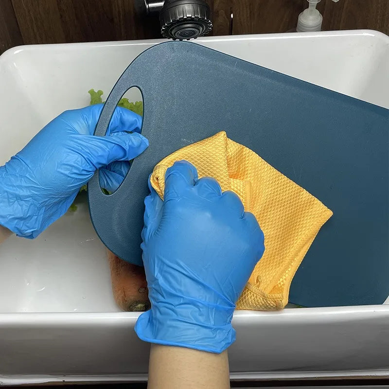 A person wearing blue nitrile gloves is using a yellow sponge to clean inside a white sink basin.