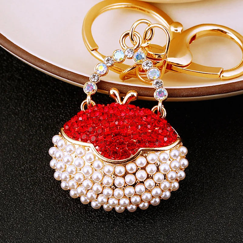 A gold-toned handbag keychain featuring a red rhinestone fruit and a pearl beaded base.