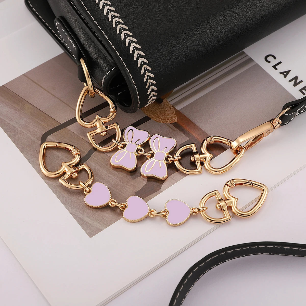 Gold- und pinke Schmetterlings-Charm-Ketten-Erweiterungen auf einer schwarzen Ledertasche.