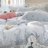 A set of three elegant ruffled duvet covers in light blue and white gingham pattern with floral embroidery on a bed.