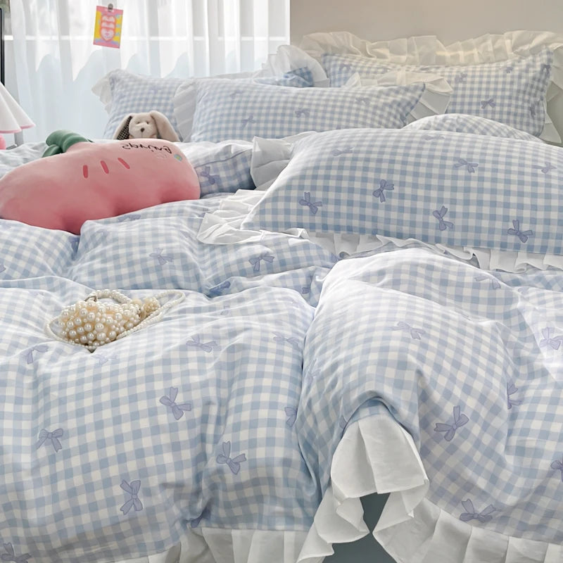 A set of three elegant ruffled duvet covers in light blue and white gingham pattern with floral embroidery on a bed.