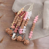 A collection of personalized silicone pacifier clips with various colors and names on a string against a beige cloth.