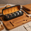 A wooden tray holds a black watch organizer case with an orange comfort pillow and several watches.