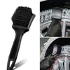 A set of black compact car wheel and tire cleaning brushes being used on a silver alloy wheel.