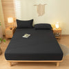 A dark gray fitted sheet is laid out on a wooden bed frame in a bright bedroom setting.